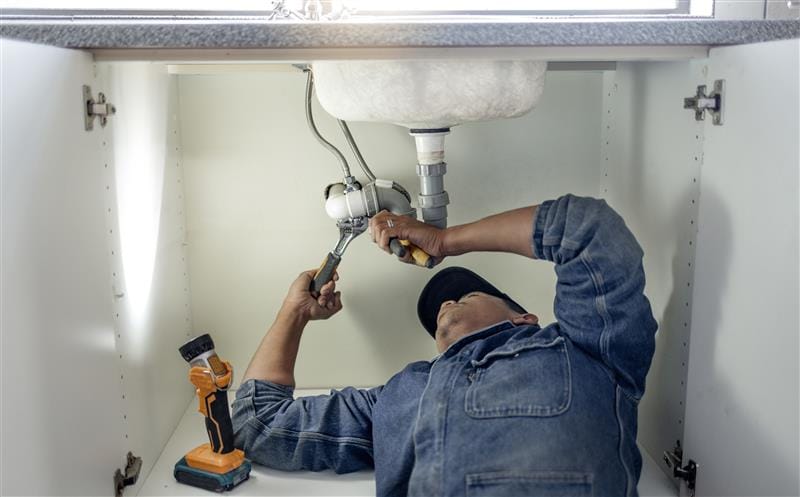 Plumber repairing pipes beneath a bathroom sink in Highland
