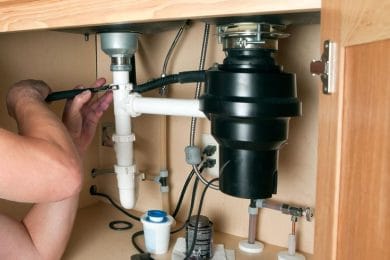 Plumber repairing a garbage disposal beneath a kitchen sink in Highland