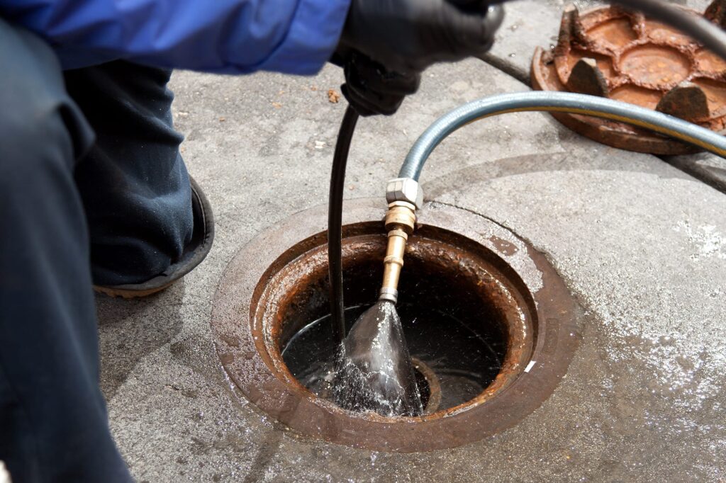 Plumber hydro jetting a sewer line through a manhole in Highland