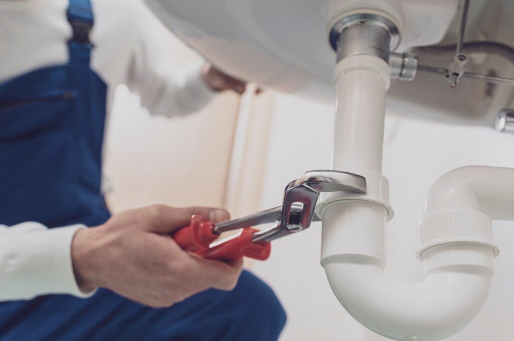 Plumber repairing a white drain pipe beneath a sink in Highland