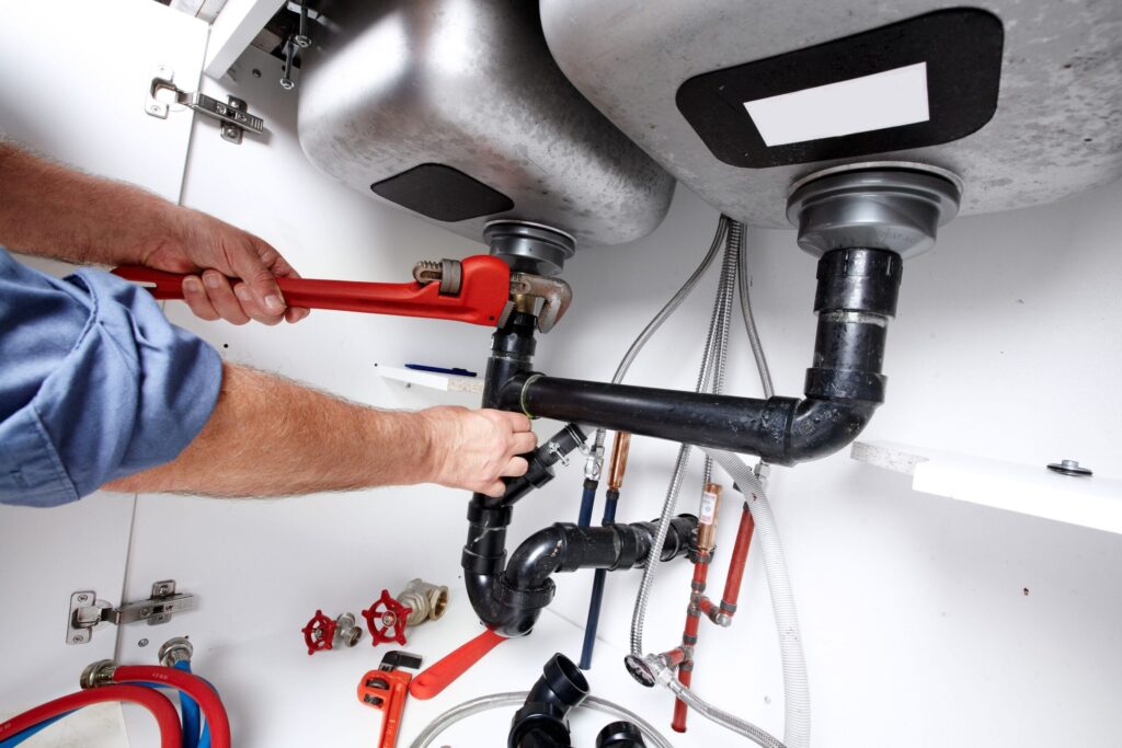Plumber repairing drain pipes beneath a kitchen sink in Highland